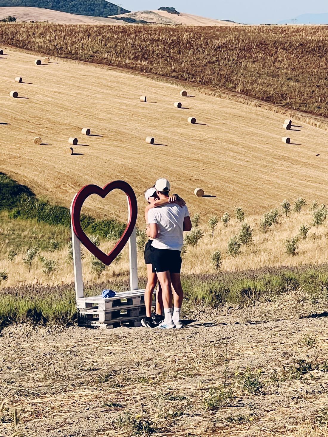 Lovisa och Mattias kramas vid det stora hjärtat på ett sädesfält