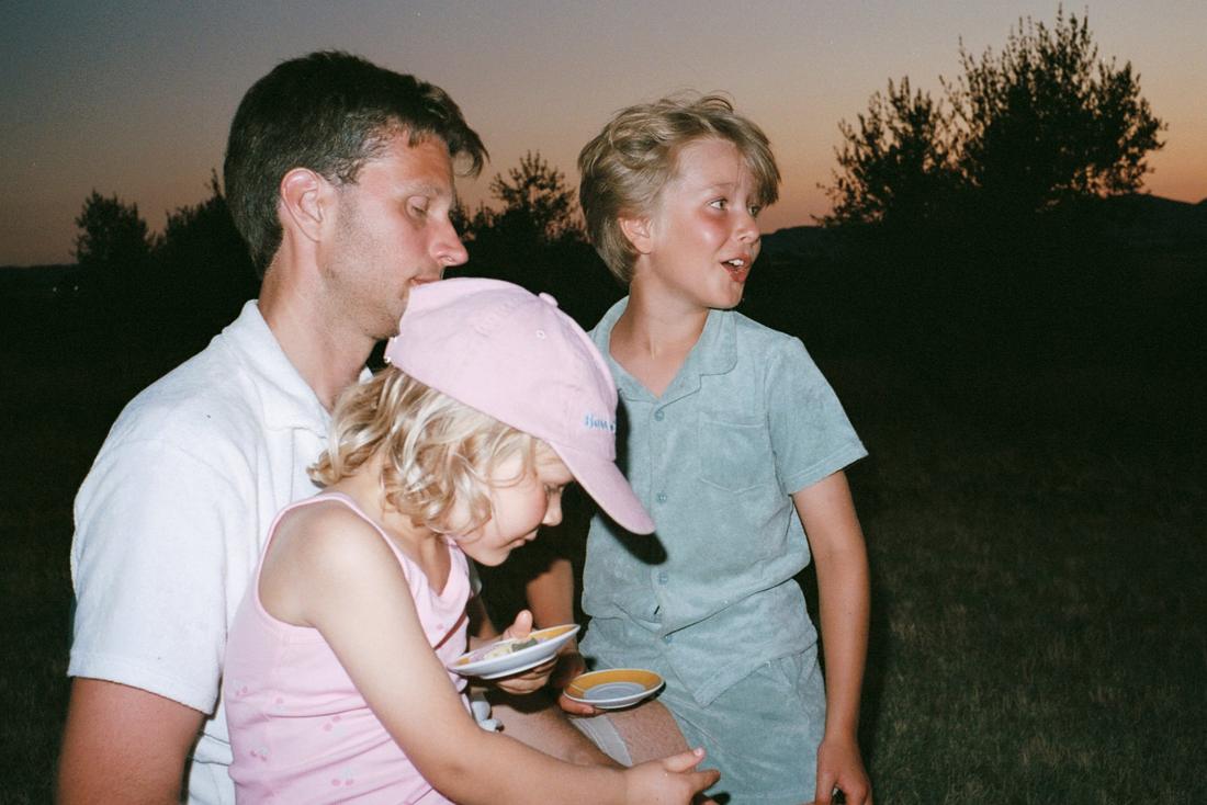 En pappa med en liten flicka i rosa keps och en pojke i skymningen