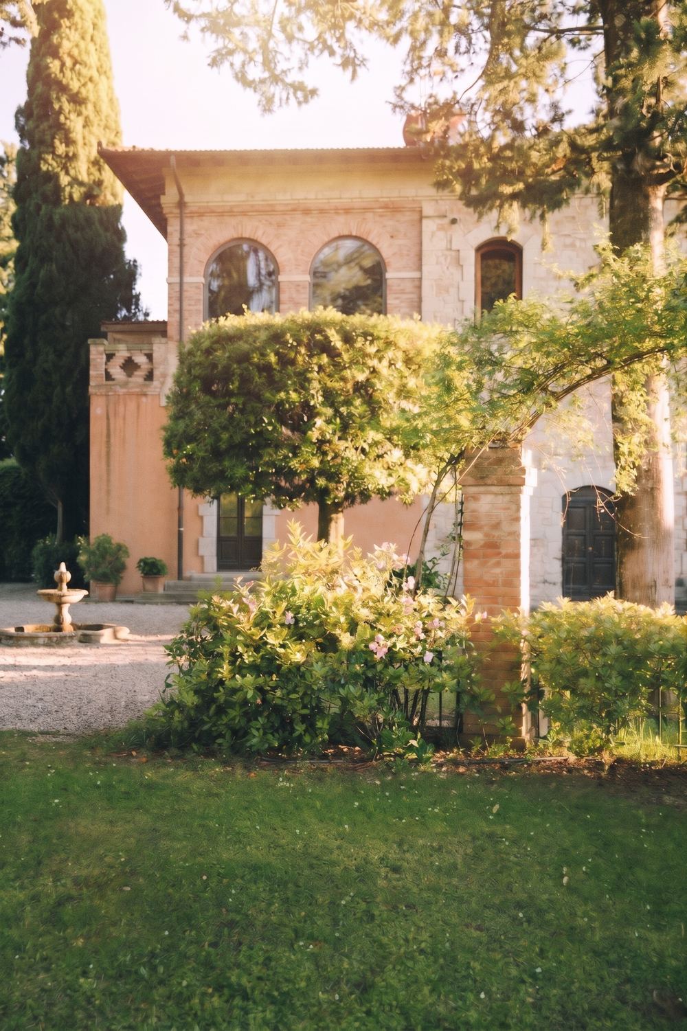 Gårdens villa i rosa puts och tegel i kvällssol, med cypresser och en trädgård med fontän